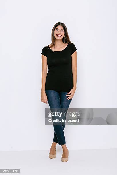 full length front view of young woman standing legs crossed looking at camera smiling - white jeans fotografías e imágenes de stock