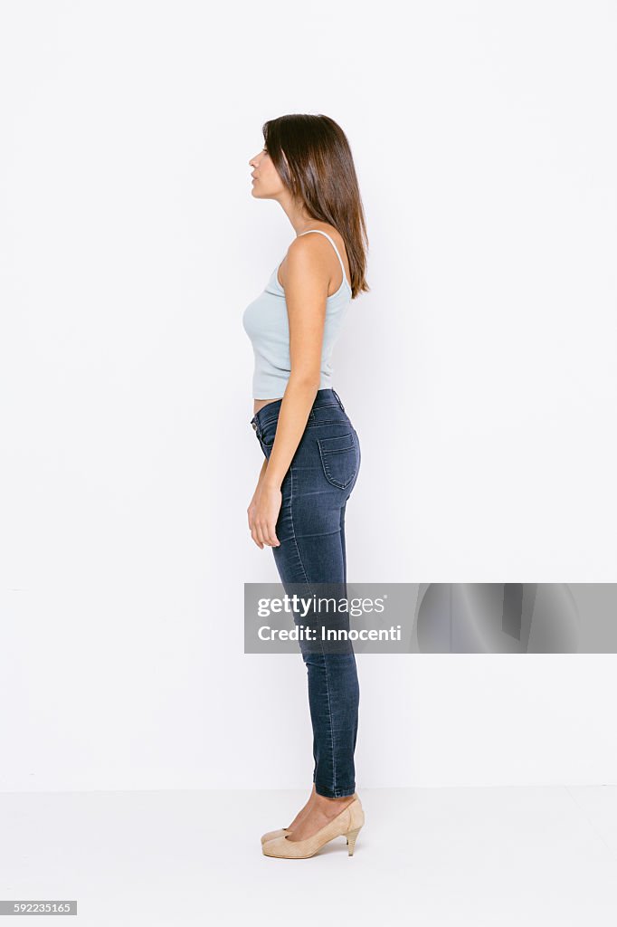 Full length side view of young woman wearing vest and skinny jeans