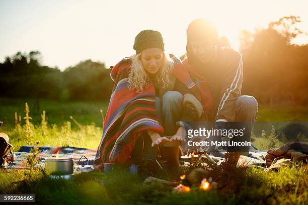 young camping couple warming hands by campfire at dusk - lincoln england fotografías e imágenes de stock