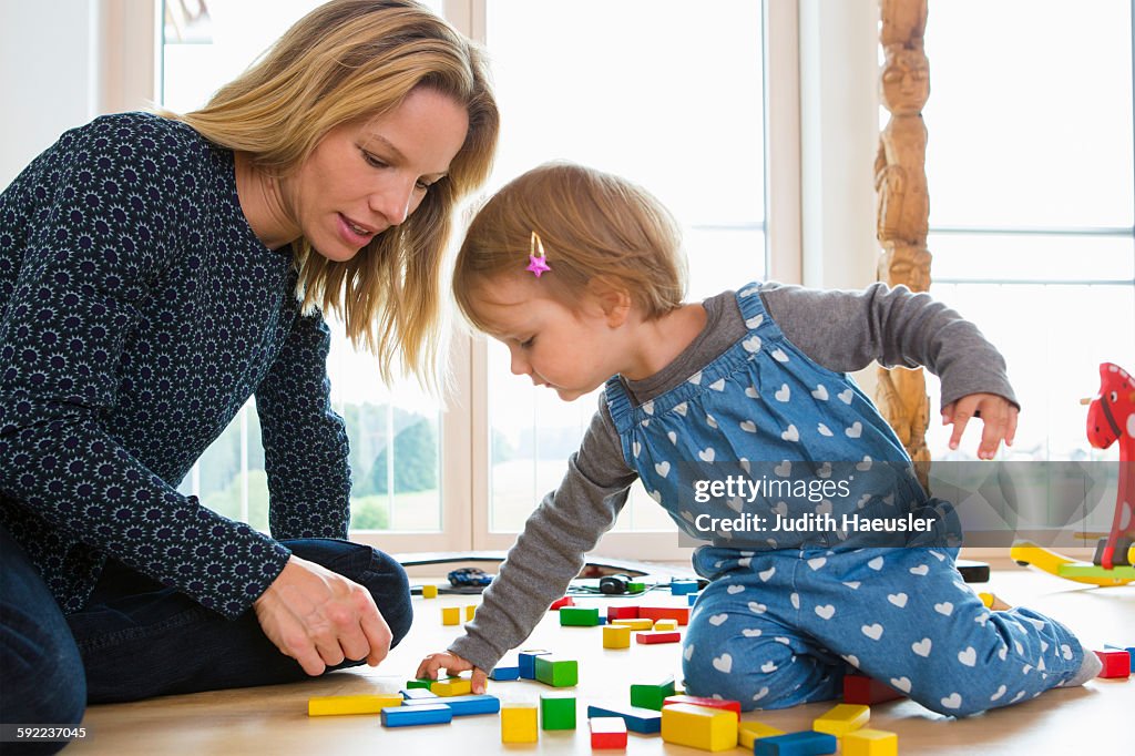 Female toddler and mother playing with building bricks on living room floor