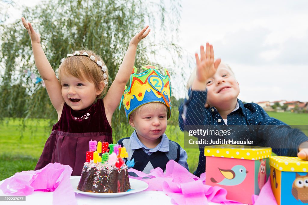 Female toddler and two young brothers at birthday party in garden