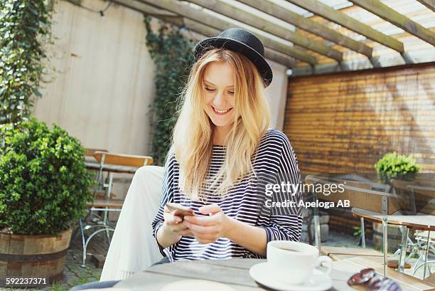 smiling young woman wearing hat using phone while having coffee at cafe - table setting design scandinavian bildbanksfoton och bilder