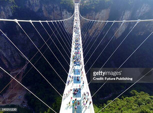 Tourists walk on the glass-floor suspension bridge on the first day of its trial operation on August 20, 2016 in Zhangjiajie, China. The...