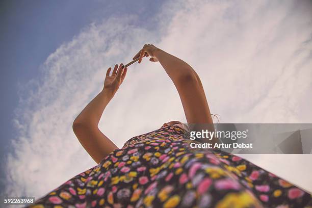 girl taking pictures with smartphone visiting the cap de creus region in costa brava taken from below view with the sky and colorful dress. - multi colored skirt stockfoto's en -beelden
