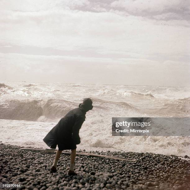 Woman throws one of the many beach pebbles in to the rough sea on the Sussex coast. Circa 1961.