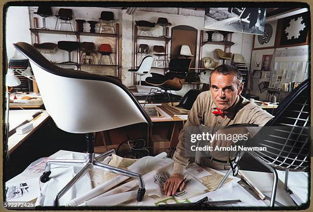 Portrait of American designer Charles Eames as he poses, his arm on one of his chairs, which sits atop a table in his studio, Venice, California,...