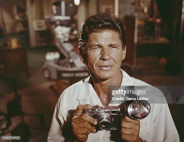 Portrait of American actor Charles Bronson as he poses on set, with a camera in his hands, circa 1958.