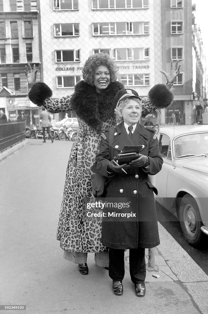 Model Lorne Lesley wearing a long leopard skin coat with fur collar standing behind a traffic warden February 1975