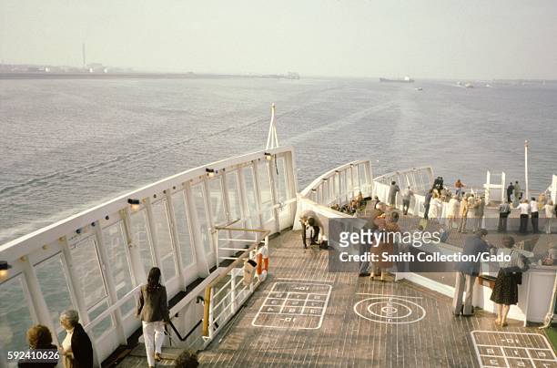 Travelers gather on the aft deck of the Cunard Line's Queen Elizabeth 2 cruise ship, where courses for various games have been painted, at sea, 1975....