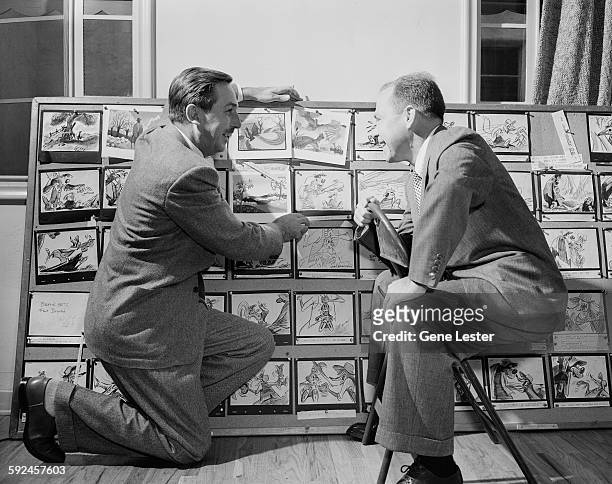 American movie producer, artist, and animator Walt Disney and musician Johnny Mercer look at story boards from Disney's 'Soug of the South' movie,...
