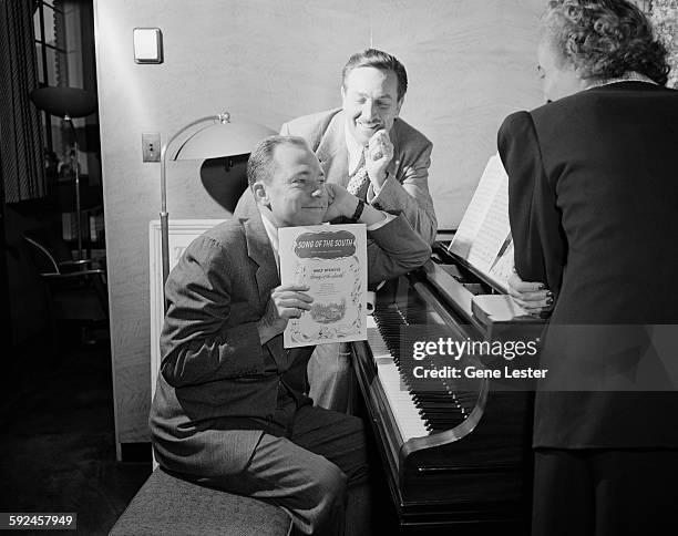 Watched by American movie producer, artist, and animator Walt Disney , musician Johnny Mercer sits at a piano and holds up the sheet music from...