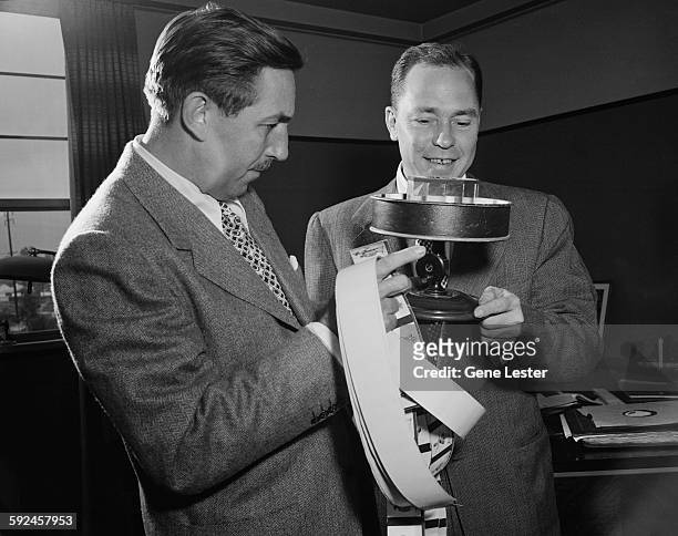 American movie producer, artist, and animator Walt Disney and musician Johnny Mercer look a hand-crank animation projector, called a praxinoscope,...