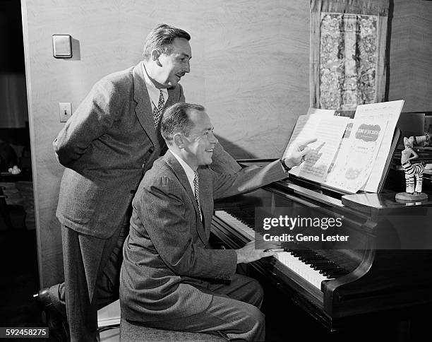 Watched by American movie producer, artist, and animator Walt Disney , musician Johnny Mercer plays piano from the sheet music of Disney's 'Soug of...