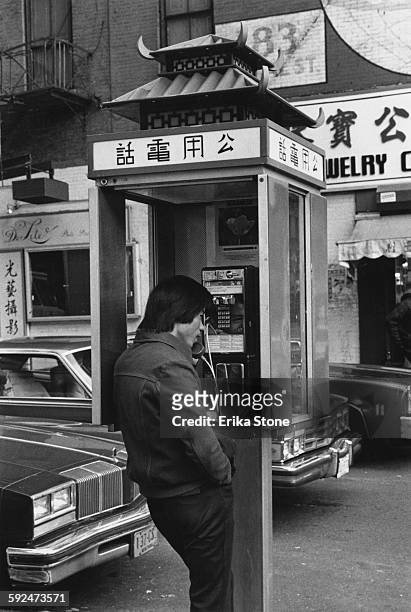 Man using a phonebooth with a Chinese-style roof in Chinatown, New York City, circa 1975.
