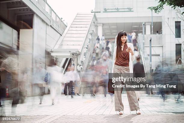 pretty young lady using smartphone on busy street - personas en el fondo fotografías e imágenes de stock