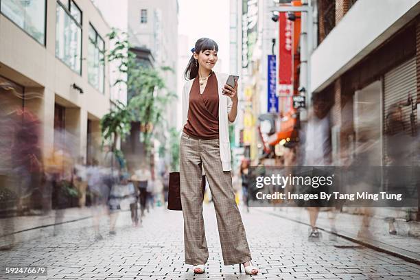 pretty young lady using smartphone on busy street - full length photos et images de collection