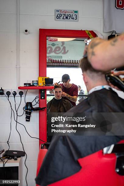 Client Alex watches in the mirror as Barber Will trims his hair.