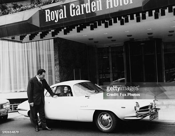 Racing driver Jochen Rindt at the wheel of his new Alfa Romeo Giulia SS car, talking to a doorman as he arrives at the Royal Garden Hotel, London,...