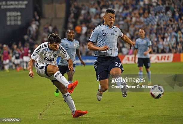 Mid-fielder Nicolas Mezquida of the Vancouver Whitecaps FC takes a shot on goal against mid-fielder Roger Espinoza of Sporting Kansas City during the...