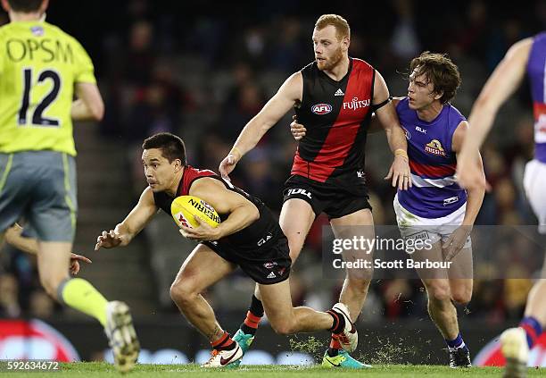 Mathew Stokes of the Bombers runs with the ball as Adam Cooney of the Bombers looks on during the round 22 AFL match between the Essendon Bombers and...