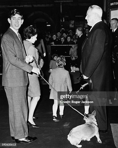 Prince Charles holding a pet corgi on a leash, with Princess Margaret and her son Viscount Linley in the background, arriving at Liverpool Street...