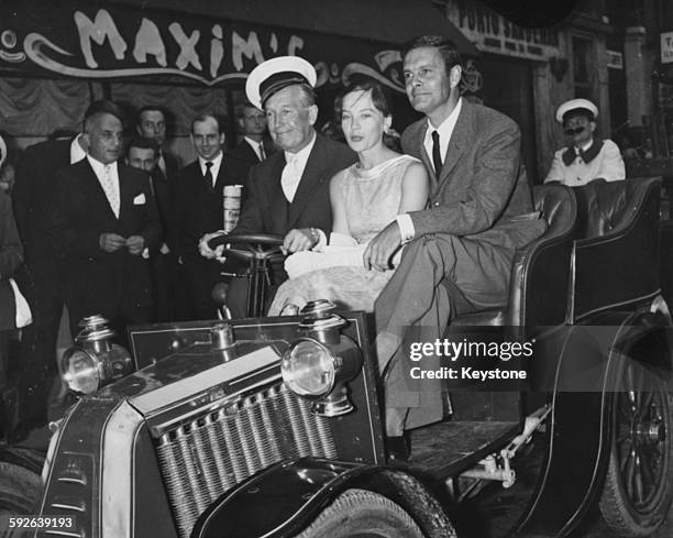 Actors Maurice Chevalier, Leslie Caron and Louis Jourdan riding in an old fashioned motor car as they arrive at a reception for their film 'Gigi' at...