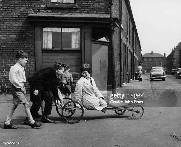 Actress Rita Tushingham being pushed around on a wheeled cart by a group of children, filming scenes for 'A Taste of Honey', Liverpool, 1960.