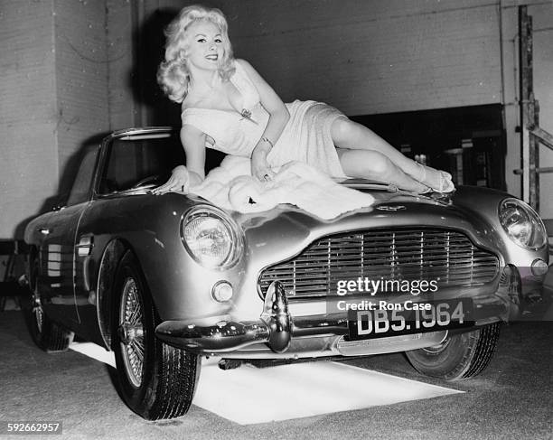Actress and model Barbara Roscoe lying across the bonnet of the new Aston Martin DB5 car, at the Motor Show in Earls Court, London, October 15th 1963.