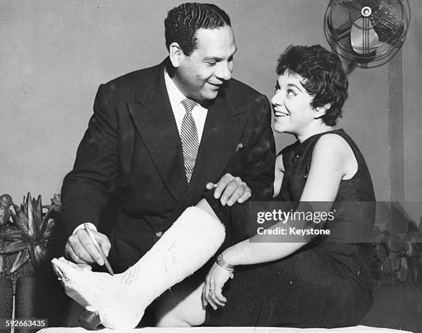 Bandleader Edmundo Ros signing the plaster cast of singer Serenella, who broke her leg on stage in Madrid, during a trip to London, September 19th...