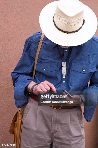 man in cowboy hat looking down at two smartphones - bolo stock pictures, royalty-free photos & images