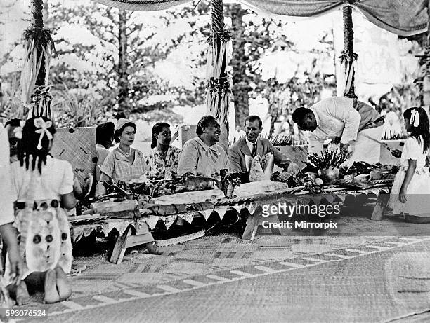 Queen Elizabeth II and Prince Philip with the Queen of Tonga at a feast at which a roasted pig was placed in front of every person, during the Royal...