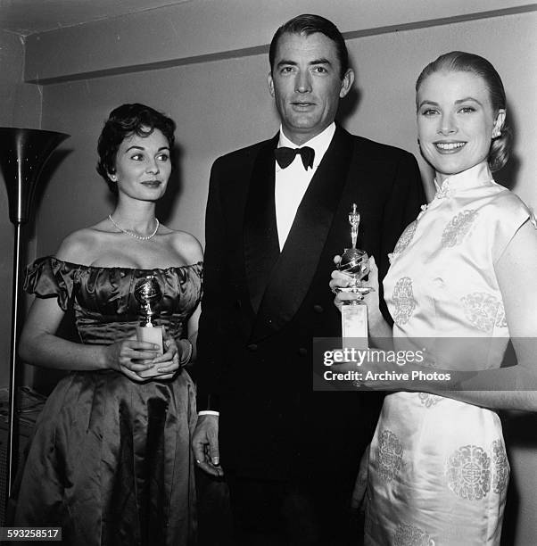 Actresses Jean Simmons and Grace Kelly holding their awards, with Gregory Peck, at the Foreign Press Awards, or the Golden Globes, in Hollywood, 1956.