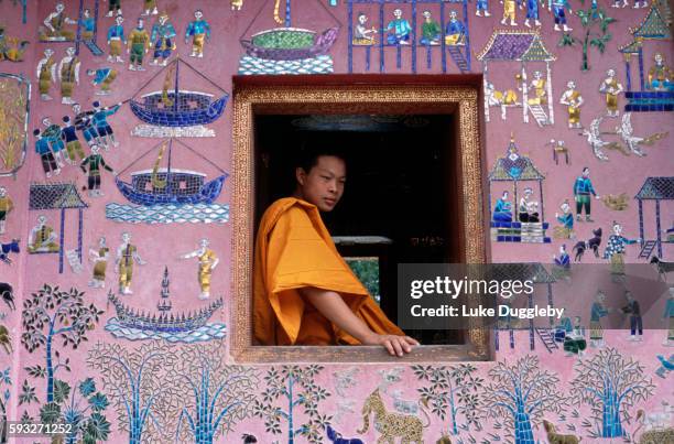 a monk in a saffron yellow robe sitting at an open window in a temple - laos stock pictures, royalty-free photos & images