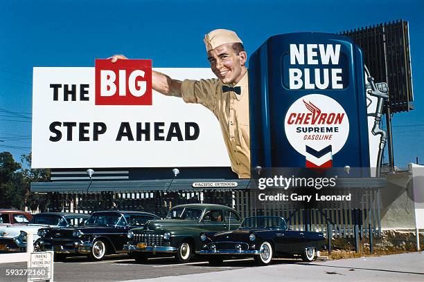 Chevron Billboard with a gas station attendant with old cars parked in front in 1958 in Los Angeles, California. 19590's Chevron Billboard with old...