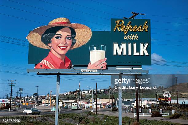 Milk billboard with a smiling woman in straw hat holding a glass of milk, above a street in 1967 in San Diego, California. 1950's billboard woman in...