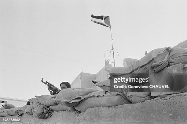 Fedayin fighter holds an AK-47 rifle as he mans a bunker, below a flying Palestinian flag, at a military base of the Fatah, a faction of the...