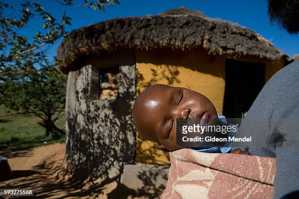 Ten month old baby Mpho who is HIV positive sleeps on the back of his mother Mathato Notsi while she sweeps her yard. He had just received the...