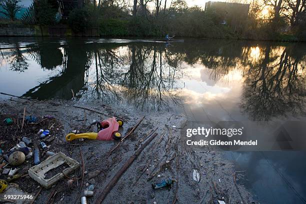 Canoeist rows along the River Lea refelcted in a beautiful Spring sunset, but oblivious to a floating mass of litter and pollution. This is in...