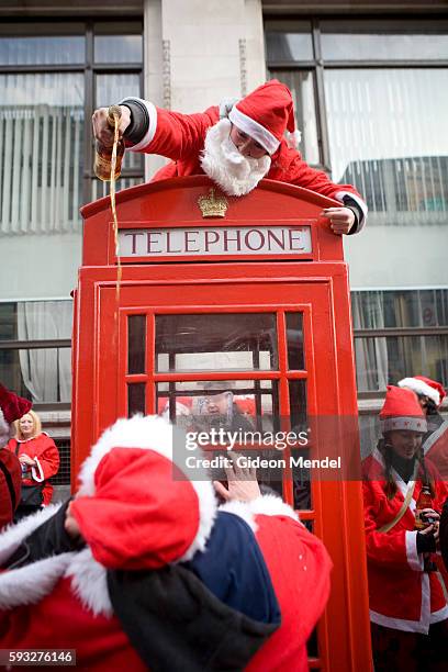 Santa pours brandy from the top of a telephone box into the mouths of other eager Santas during the London SantaCon event. SantaCon is a mass...