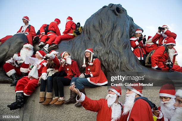 Various bawdy Santas occupy a lion at Trafalgar Square many of them taking photographs during the London SantaCon event. SantaCon is a mass gathering...