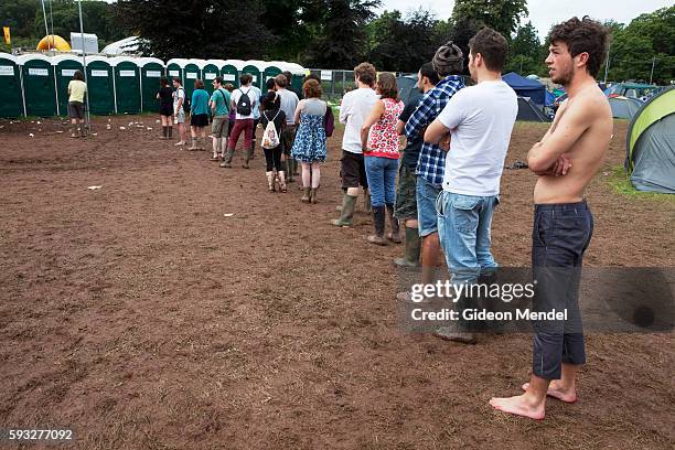 Long queue of music fans wait to use the toilets at the Green Man Festival on a trough of brown mud after hours of constant rain. This is an...