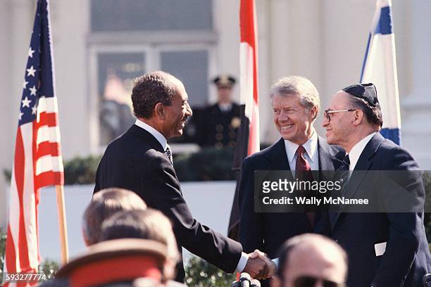 President Jimmy Carter watches as Egyptian President Anwar Sadat and Israeli Prime Minister Menachem Begin shake hands on the north lawn of the White...