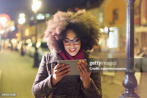 smiling young woman using digital tablet on streets by night - browsing the internet stock pictures, royalty-free photos & images