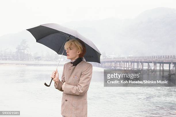 David Sylvian Japan) standing with umbrella at the riverside in rainy Arashiyama Kyoto, Kyoto, February 1981.
