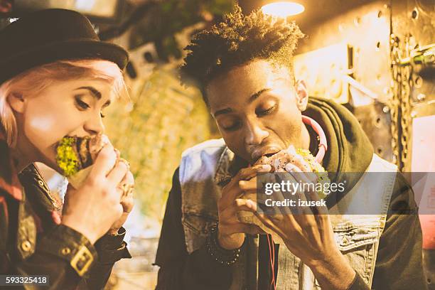 afro american guy eating burger with his female friend - pub food stock pictures, royalty-free photos & images