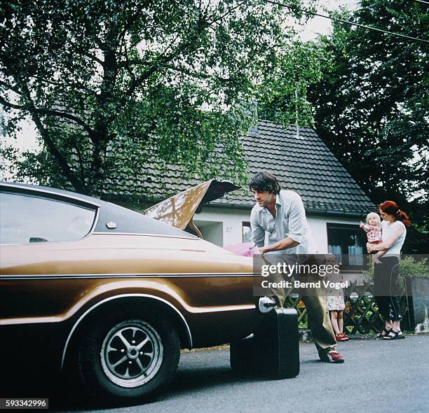 father loading luggage into car, mother with daughters behind him - baby boot stock pictures, royalty-free photos & images