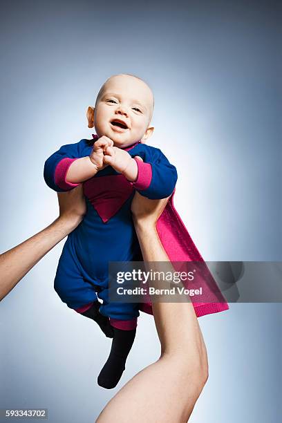 woman holding up baby in superman costume - superman stock-fotos und bilder