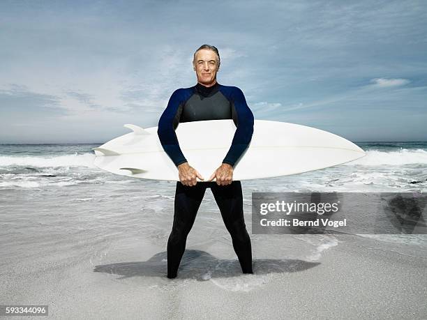 man standing on beach holding surfboard - surfer portrait fotografías e imágenes de stock