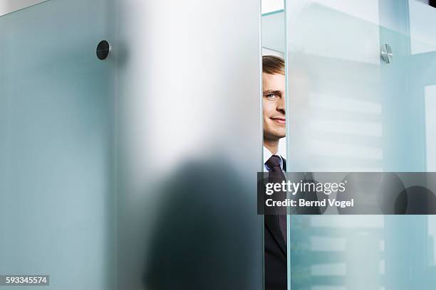 businessman peeking behind glass - frosted glass stockfoto's en -beelden