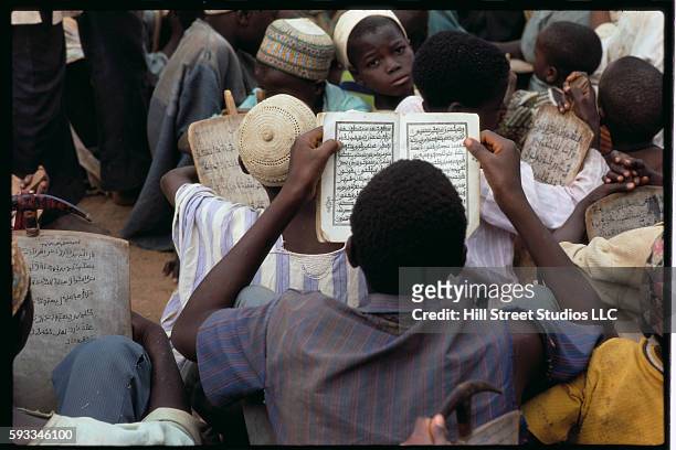 Group of young students in Nigeria sits on the ground and studies verses from the Koran.